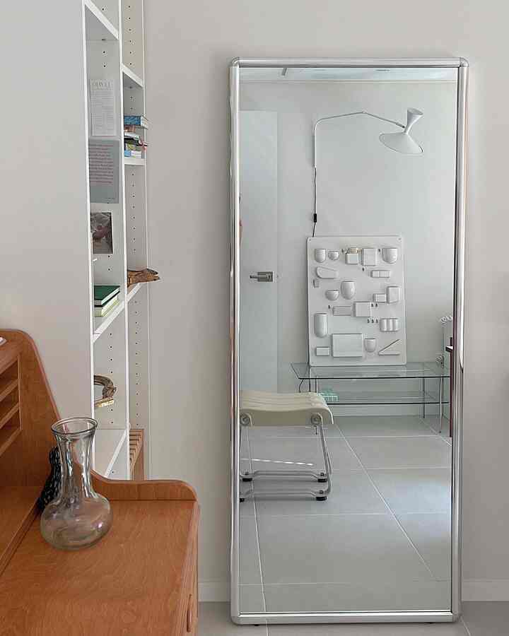 A simple and natural space featuring white walls and floors, a natural wood desk, and a large full-length mirror