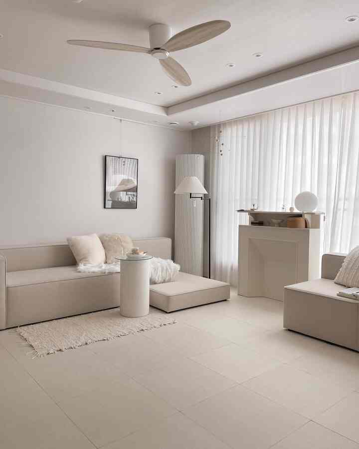 White and beige toned living room featuring a beige sofa, rug, ceiling fan, and floor lamp in a natural modern interior