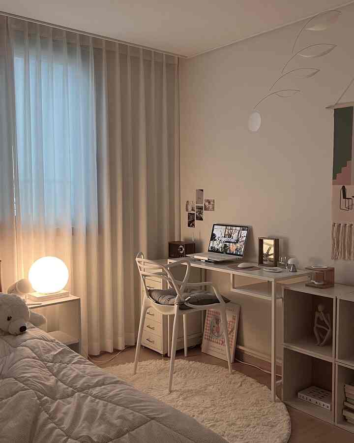 A cozy white and wood tone small bedroom featuring a simple desk, chair, and round rug for a home office setup