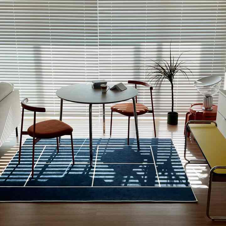 ホワイトとネイビーのトーンが特徴的なリビング、丸いダイニングテーブルとオレンジ色の椅子が配置されたモダンなインテリア