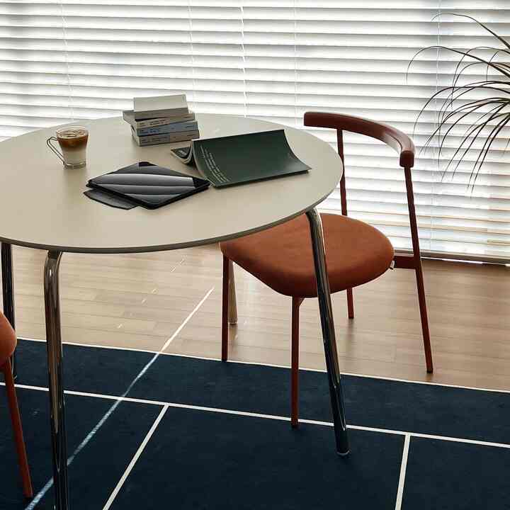 Living room with wood-tone flooring, a white round dining table, and two orange Mina chairs, featuring a clean and calm atmosphere