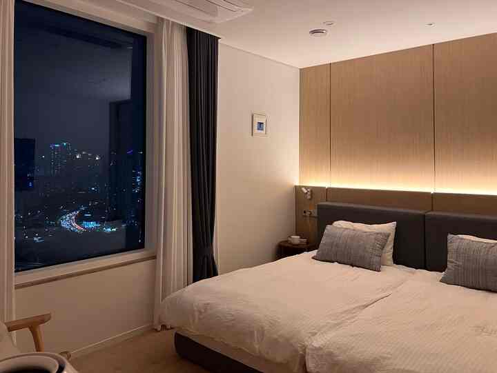 Modern bedroom with white walls and brown wood-paneled accent wall, featuring plush bed and blackout plus sheer curtains creating a hotel-like atmosphere