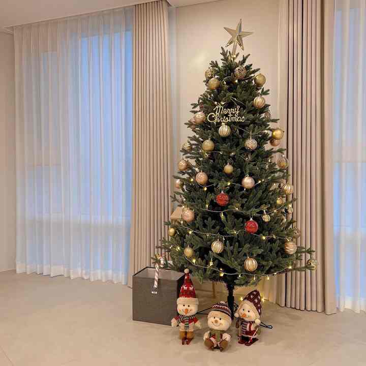 ベージュのトーンが特徴のリビングルーム、両側に二重カーテンがあり、クリスマスツリーとスノーマンドールが配置された温かみのあるインテリア