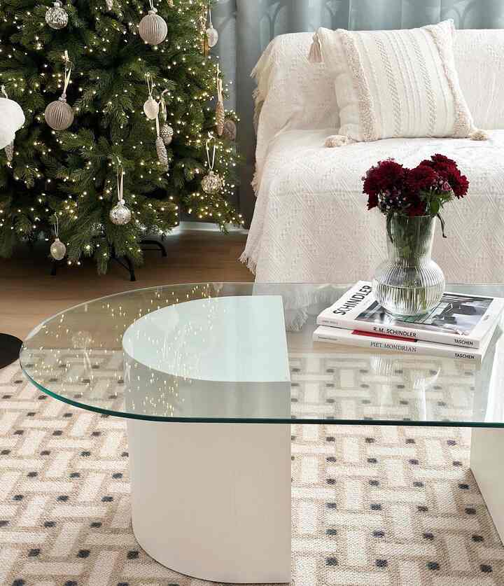 A white and gray toned living room featuring a white sofa, glass coffee table, and a decorated Christmas tree creating a cozy atmosphere