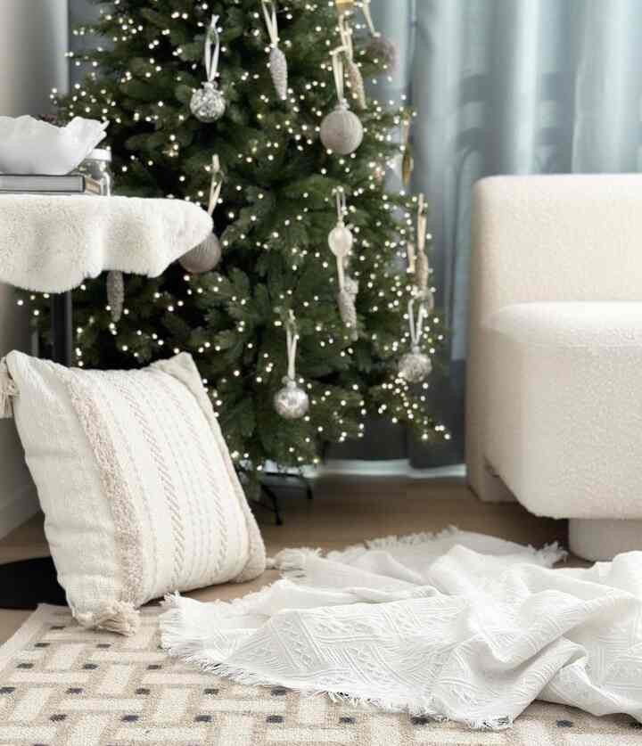A white and green living room featuring a decorated Christmas tree, cozy sofa, cushions, and throws creating a warm atmosphere