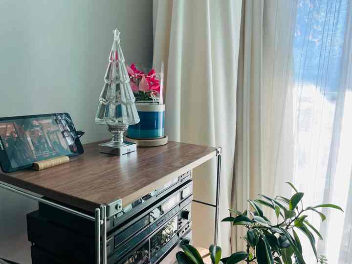 A living room corner in white and wood tones featuring a Muji shelf adorned with Christmas decor and plants, creating a cozy atmosphere