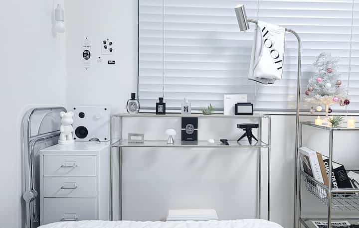 白とモノトーンの一人暮らしの部屋、きれいなメタルシェルフとフロアランプが配置されたモダンで整頓されたインテリア