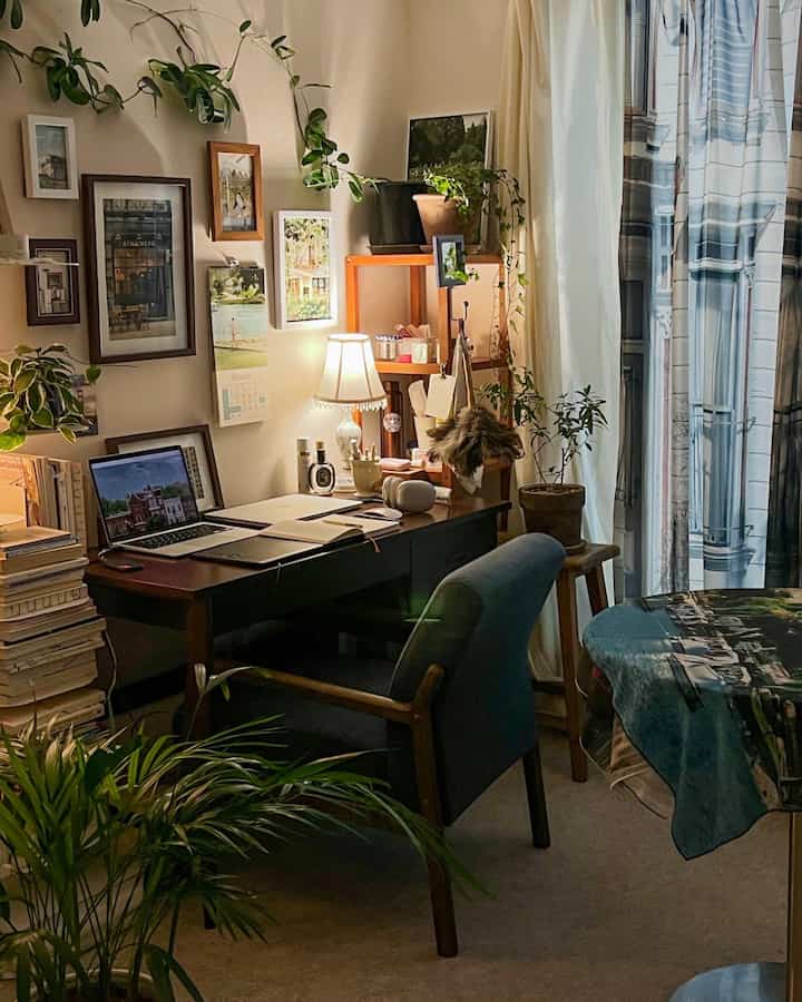 Natural toned home office space featuring wooden desk and chair, plants and curtains blending in cozy nighttime atmosphere