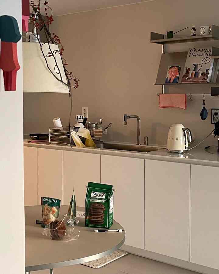 明るい白とアイボリーのトーンのキッチンスペース、SMEGの電気ケトルと丸いダイニングテーブルが配置されたミニマルなおうちカフェ風インテリア