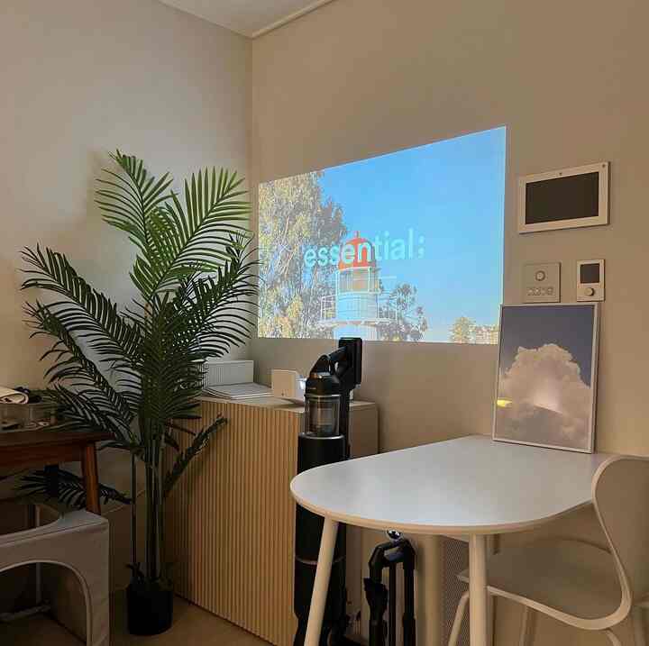 ベージュと木目調のワンルーム、ナチュラルな家具とプロジェクターが配置された雰囲気のあるホームオフィス空間