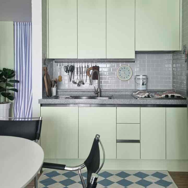 Mint-toned kitchen with white tiled backsplash, featuring sleek dining chairs and patterned rug creating a simple atmosphere