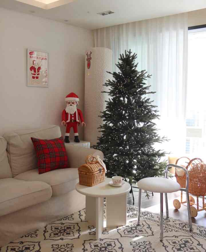Bright white-toned living room featuring beige sofa, round coffee table, and Christmas tree creating a cozy atmosphere