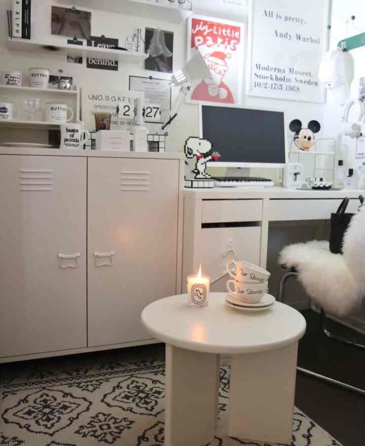 Modern compact home office in white tones with black patterned rug, white side table and desk, wall adorned with multiple framed art