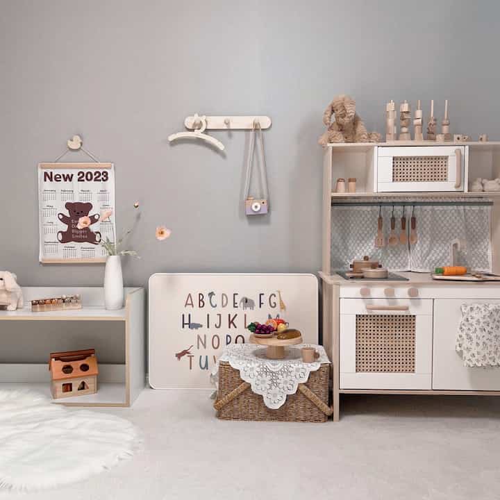 白とナチュラルカラーの子供部屋、ままごとキッチンとレースカバー付きラタンバスケットが配置された雰囲気あるインテリア