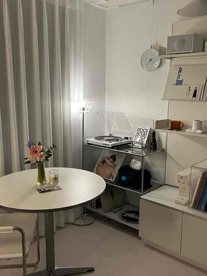 White-toned small modern home cafe space featuring a round dining table and turntable with clean decor
