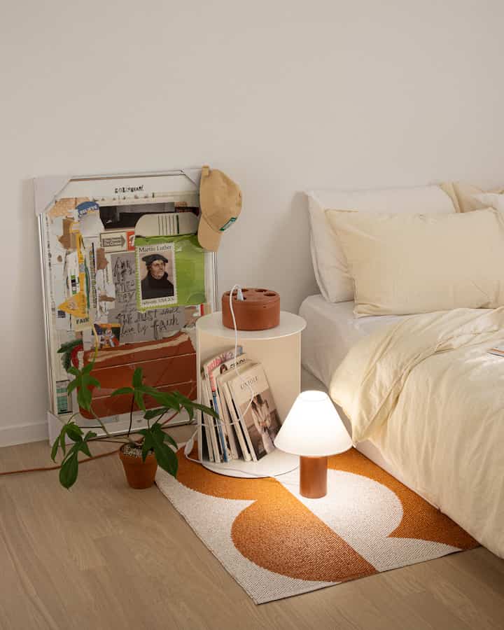 A cozy bedroom in soft beige and orange tones, featuring a bedside table with multi-tap and warm lighting
