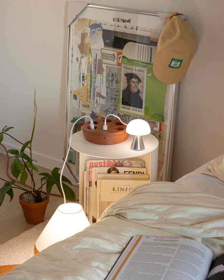 Beige bedding in a simple natural bedroom featuring a nightstand with wireless charging mushroom LED lamp and large framed collage, creating cozy atmosphere