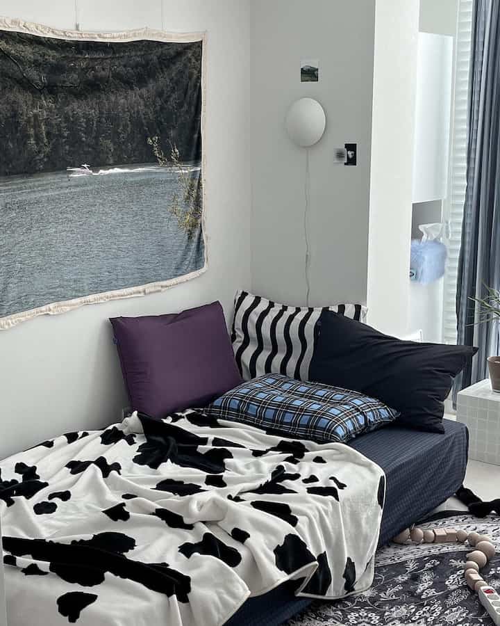 モノトーンの黒と白の色調の寝室、さまざまなパターンと色の枕とカウ柄の毛布が配置された印象的な空間