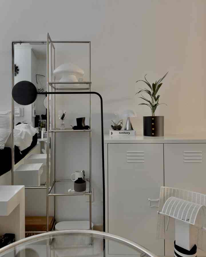 白を基調とした狭い部屋、キャビネットと全身鏡、植物、フロアランプが配置されたモダンな雰囲気のインテリア