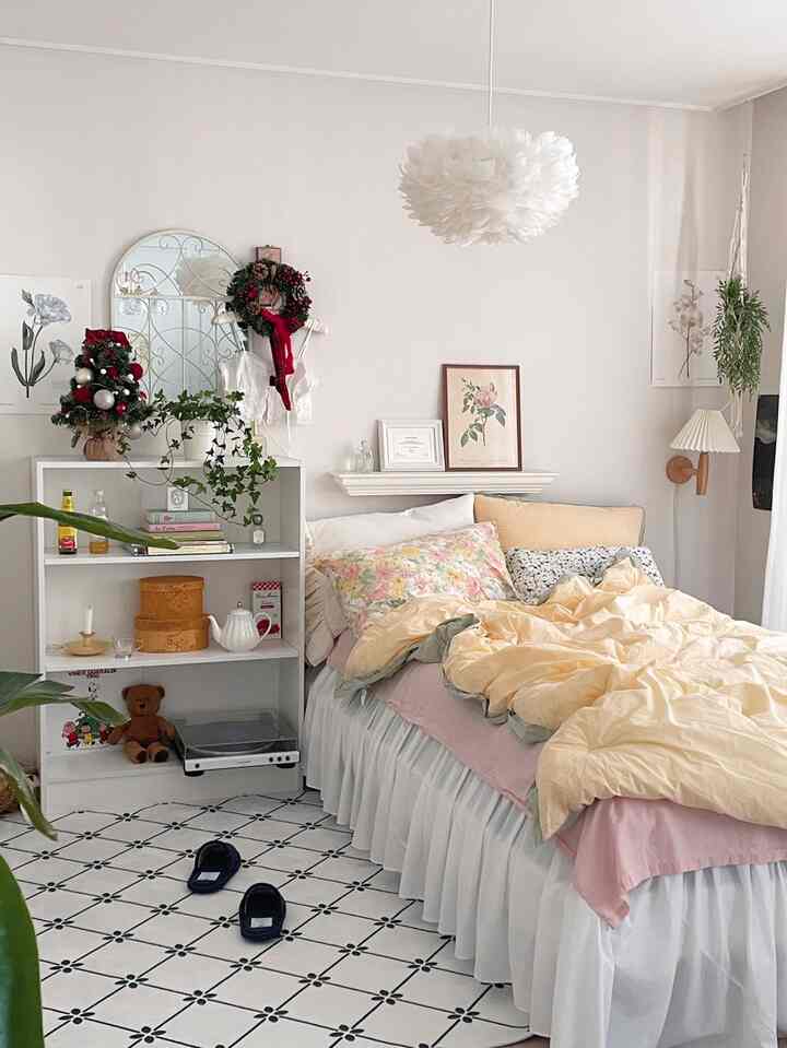 White and beige toned bedroom featuring floral pillows, bedding, a shelf, and wall decorations creating a warm atmosphere