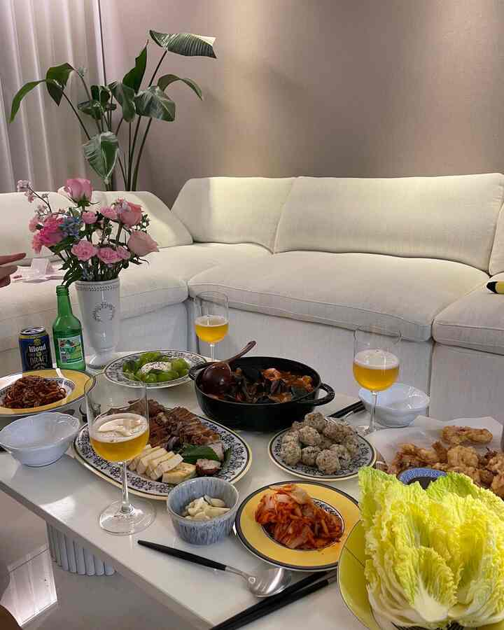 白と黄色のトーンのリビングルーム、広いコーナーソファと多彩な料理が盛り付けられたテーブルがあるホームパーティーの雰囲気のインテリア