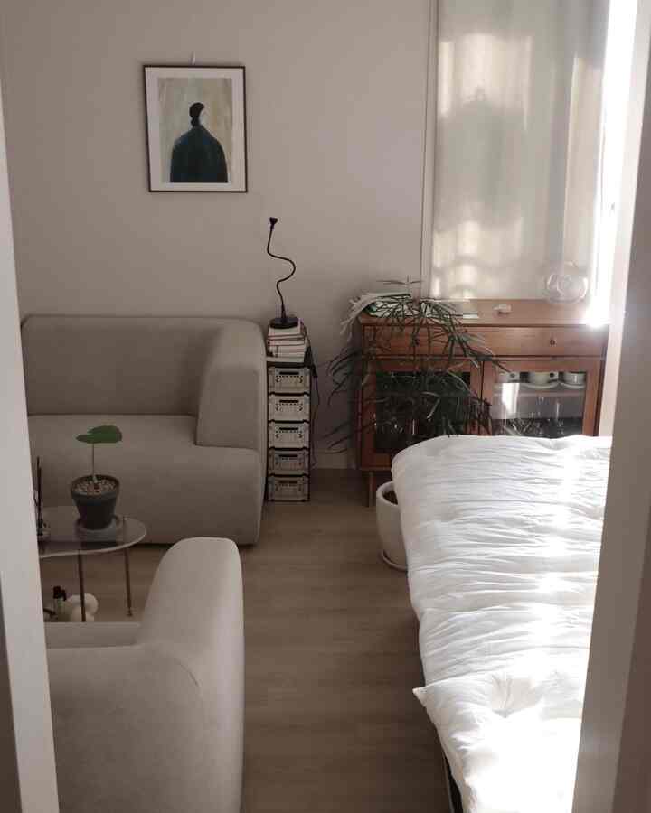 白とナチュラルな色調の寝室、ソファ、植物、掛け布団カバーが配置された雰囲気のあるインテリア