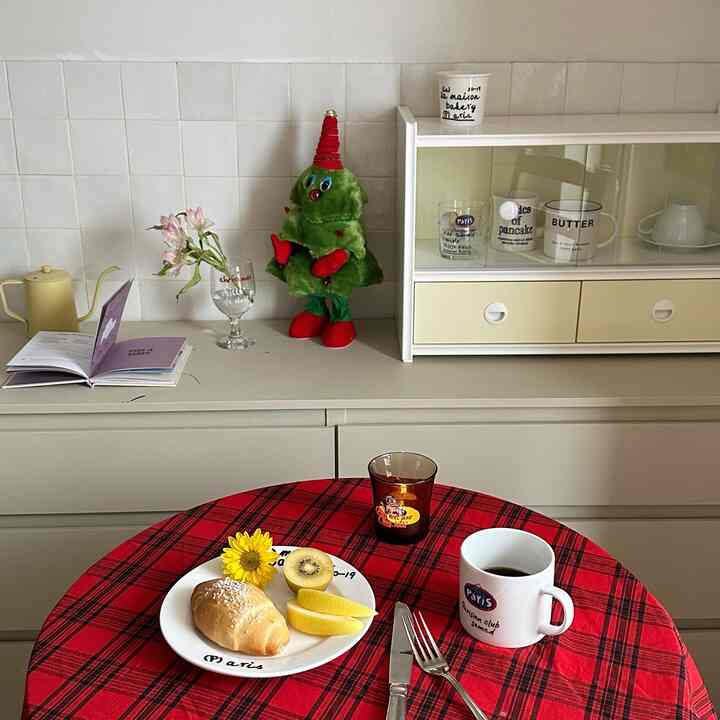 Dining room with red check tablecloth and ivory cabinet, cozy ambiance featuring Christmas doll and tableware