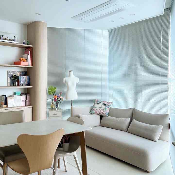 A modern and natural home office space in white and beige tones featuring a bay window sofa and aluminum blinds