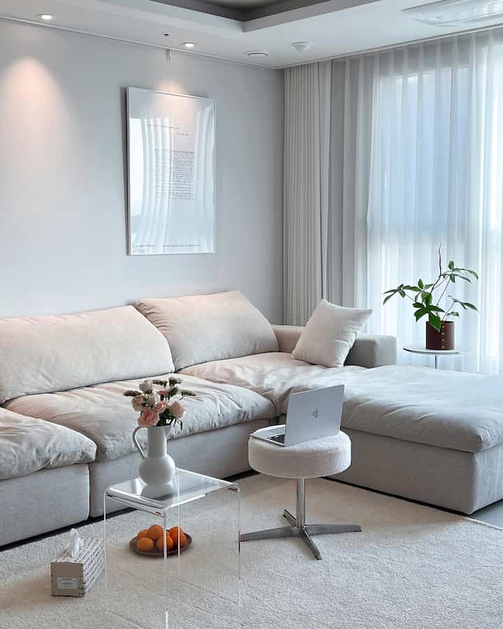Ivory and white toned living room featuring fabric sofa, transparent side table, vase with flowers, and plants in a calm healing environment