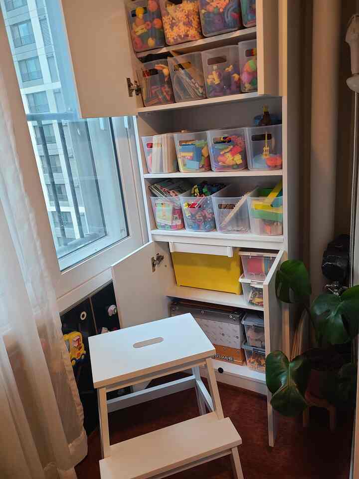 White-toned kids' room veranda featuring organized toy storage shelves and a white stool in a cozy setting