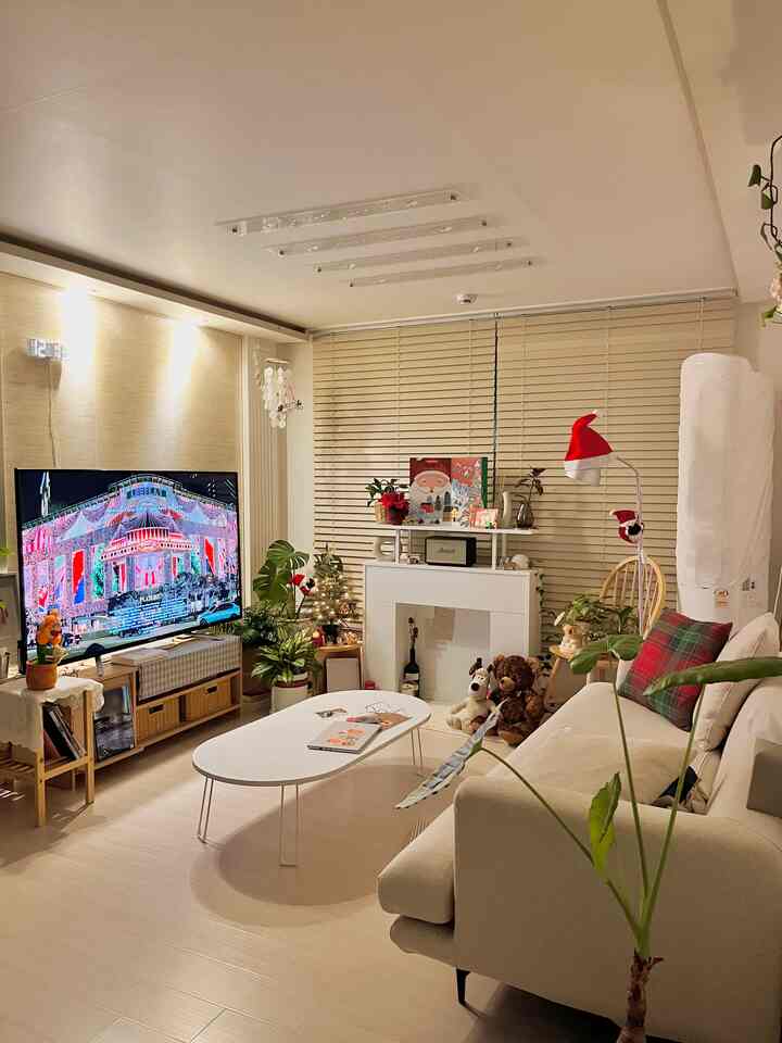 White and beige toned living room featuring white sofa and coffee table, fireplace console, and festive Christmas decor creating a cozy atmosphere