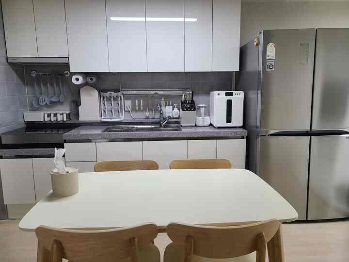 白とシルバーのトーンのキッチン、ナチュラルウッドのダイニングチェアと整理された調理器具が配置されたモダンな空間