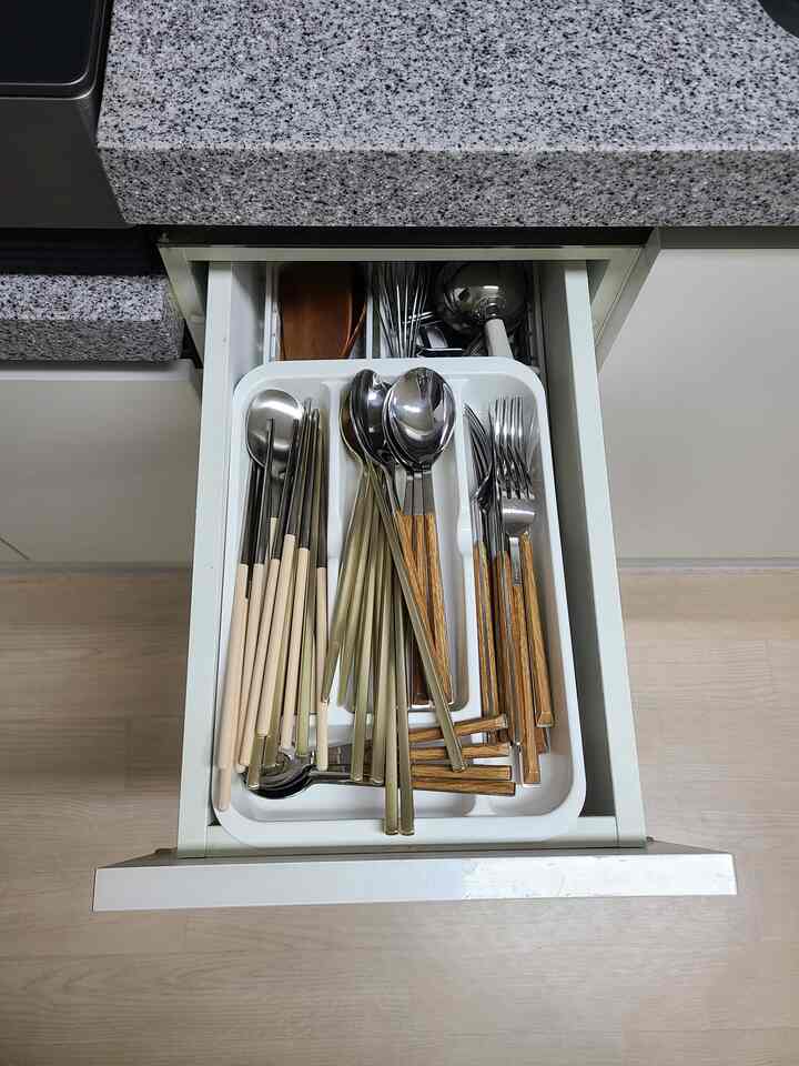 Open white cutlery tray drawer in kitchen with assorted silver and wood-handle utensils neatly organized, clean and modern setting