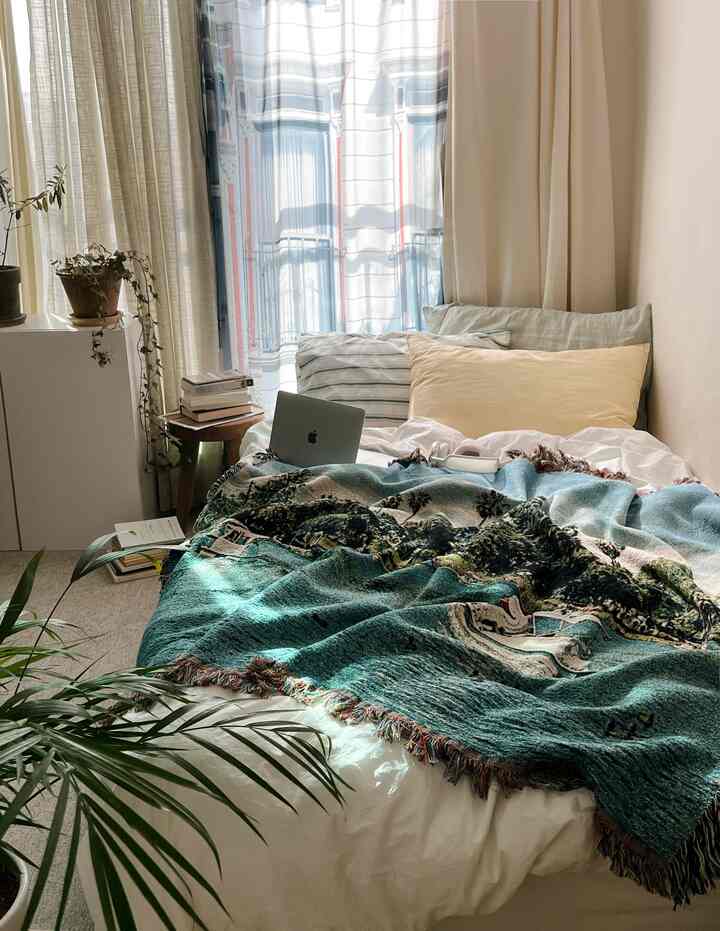 白と緑の色調の寝室、ブランケットと枕が配置された心地よい空間と自然光が差し込むカーテン