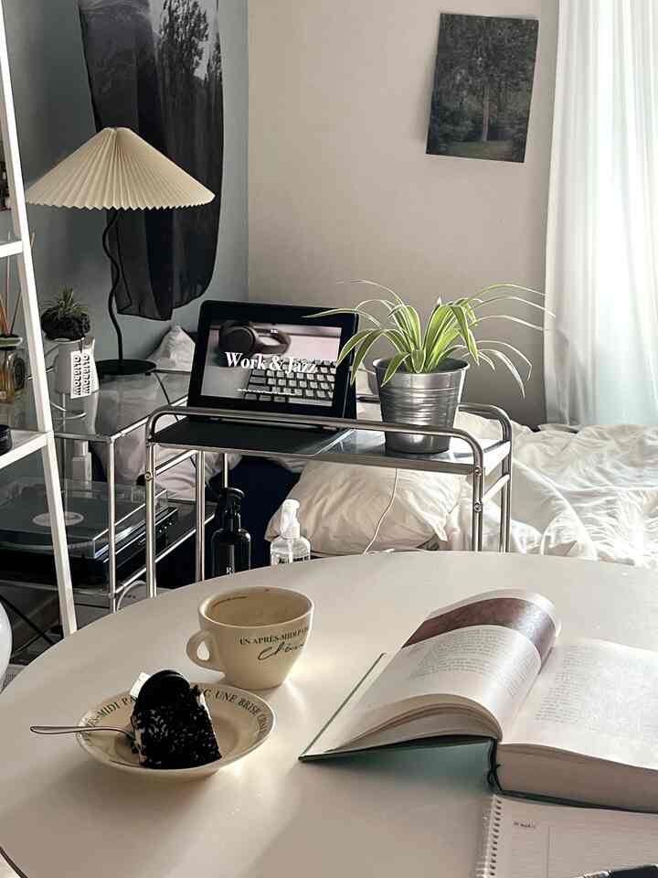 White-toned studio bedroom featuring a round dining table, plants, and cozy home office ambiance