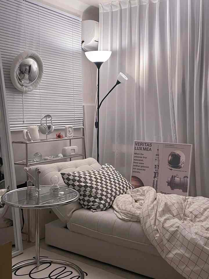 White-toned living room featuring a sofa bed with checkered cushion and floor lamp, creating a simple modern interior atmosphere