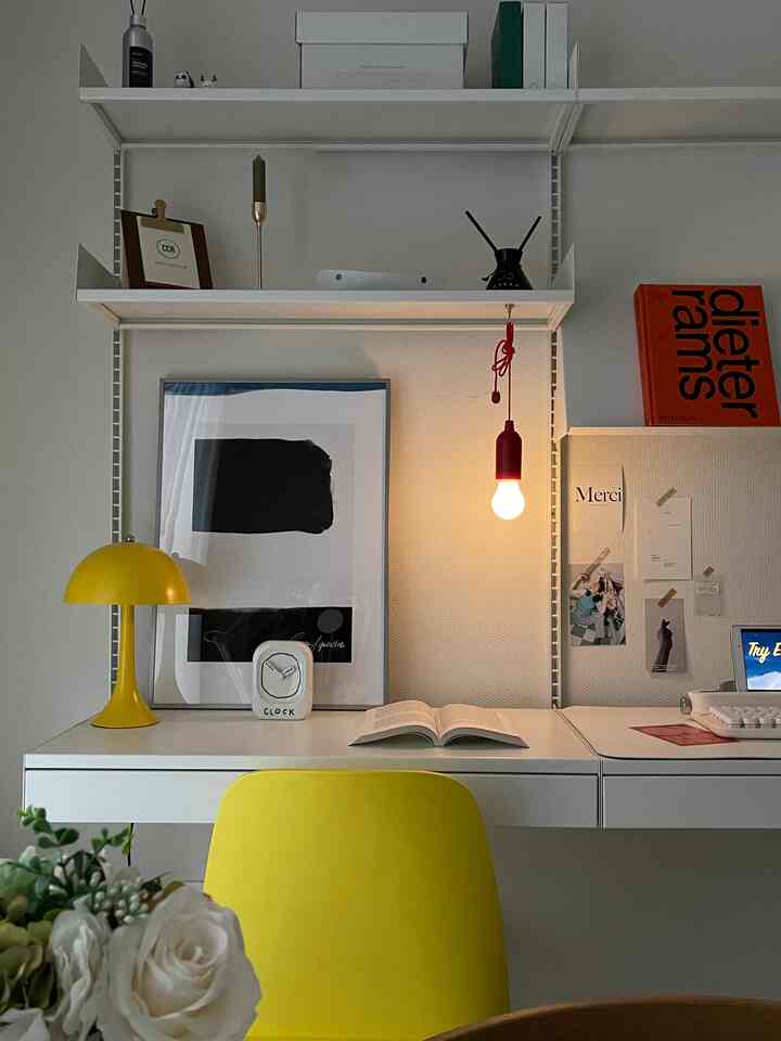 White and yellow toned home office featuring a simple desk, shelves, pendant light, and an open book for a cozy atmosphere
