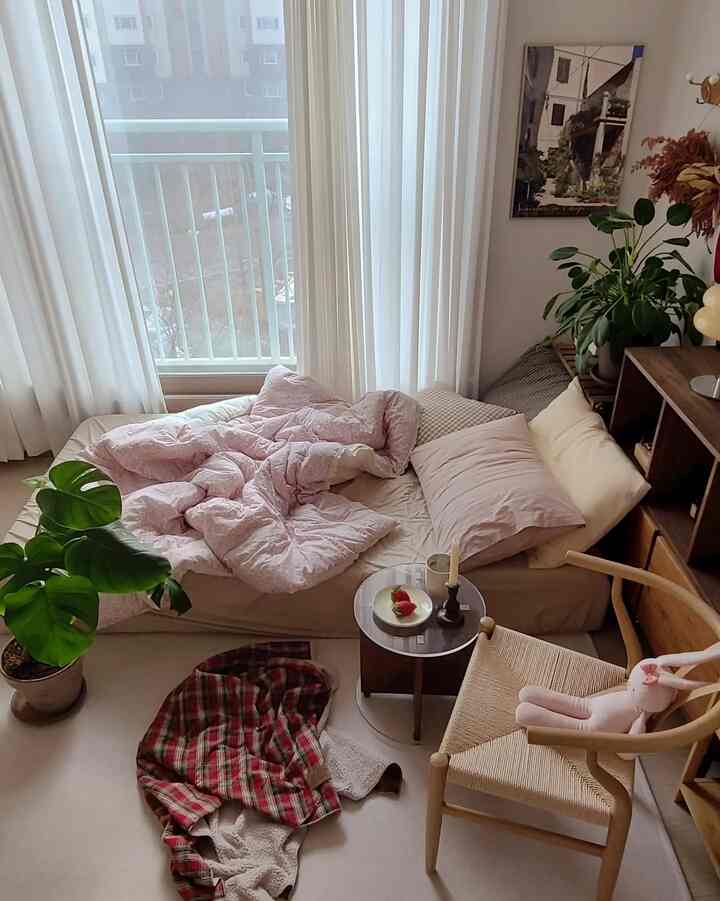 White and pink toned bedroom with natural furniture and plants arranged in a cozy space