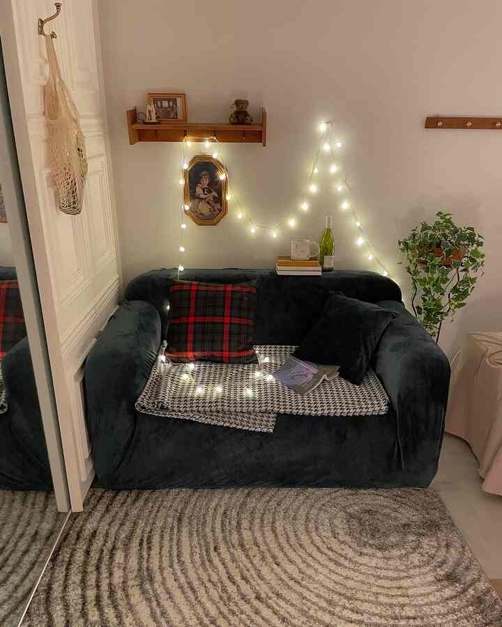 ヴィンテージ風のワンルームリビング、黒いソファと赤いチェック柄のクッション、フェアリーライトが温かみのある居心地の良い空間を演出