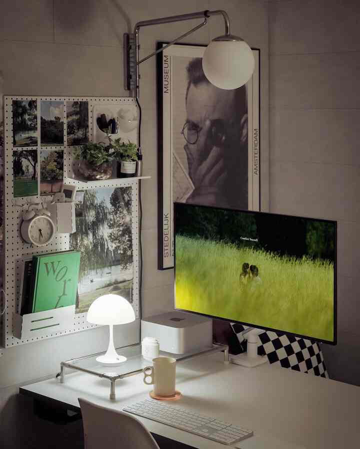 Modern home office desk in white and green tones featuring pegboard with posters and organized workspace
