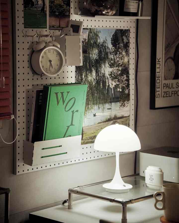 Minimal desk space featuring white pegboard wall and white table lamp