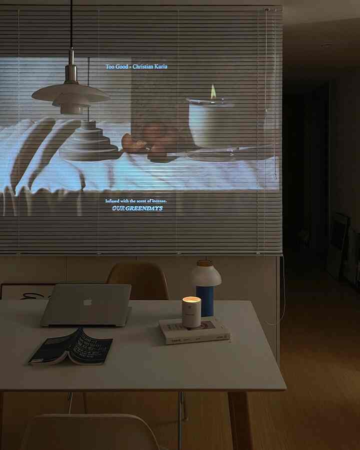 Modern minimalist home office with white blinds background, featuring a desk with laptop and lit candle creating a calm space