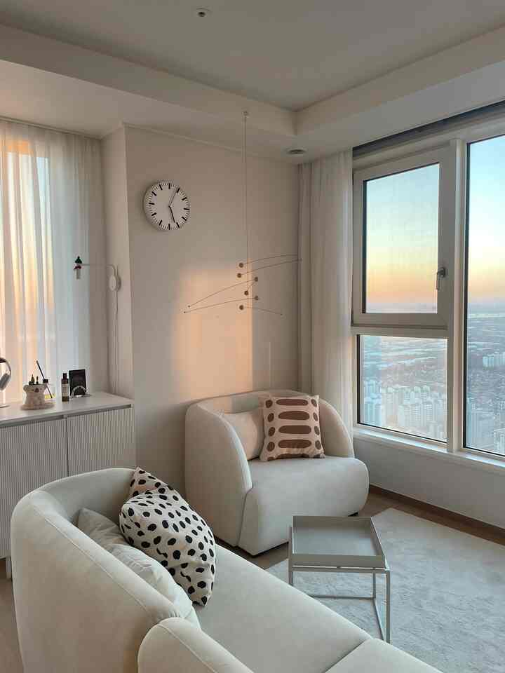 Bright ivory-tone living room featuring a round clock and two single armchairs with a modern, cozy atmosphere