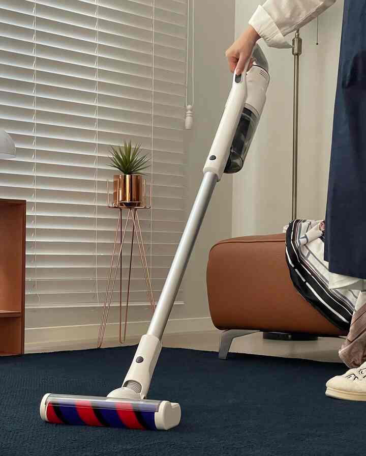 白とネイビートーンのモダンなリビング、コードレス掃除機、ブラウンソファ、金属製プラントスタンドが配置された空間