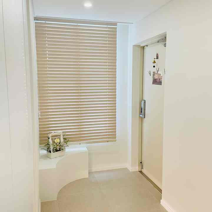 Bright and clean entrance featuring beige wood tone blinds and a white front door