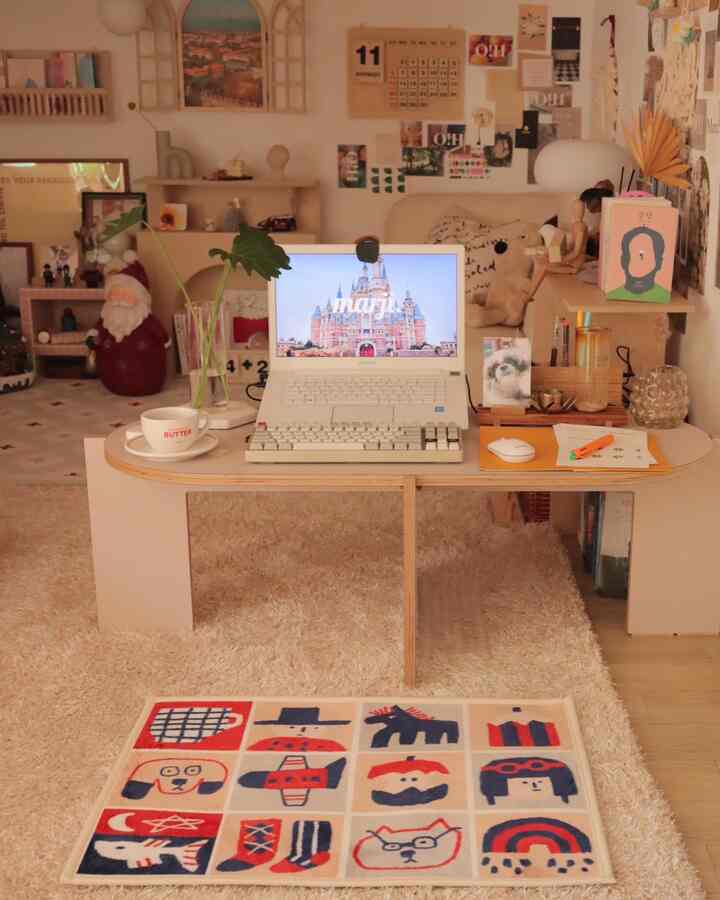 Beige and natural toned small cozy remote work space featuring a wooden desk with laptop and coffee cup, decorated with wall art and accessories
