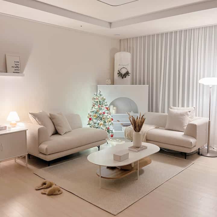 Beige and white tone living room featuring two cream fabric sofas, white coffee table, and a Christmas tree, creating a clean minimal space