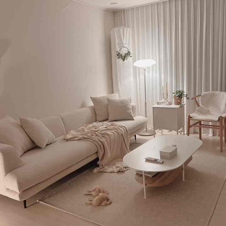 Beige-toned living room featuring a simple modern sofa and natural wood armchair in a cozy setting