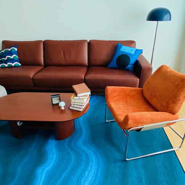 Natural modern living room featuring brown sofa, orange armchair, and blue rug with a warm, contemporary atmosphere