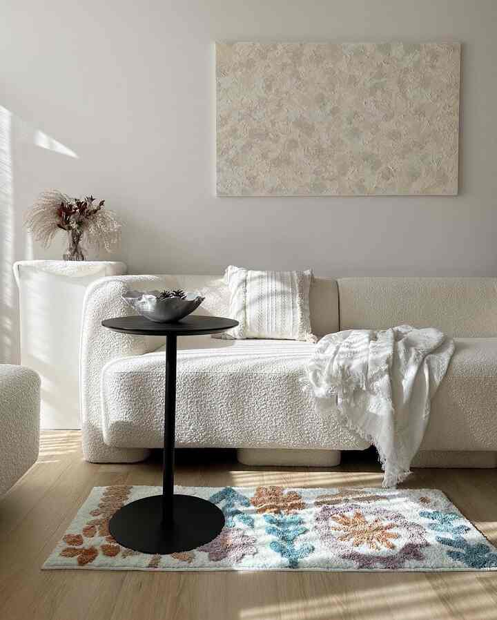 Bright white-toned living room featuring textured sofa, throw blanket, and floral pattern rug creating a natural interior atmosphere